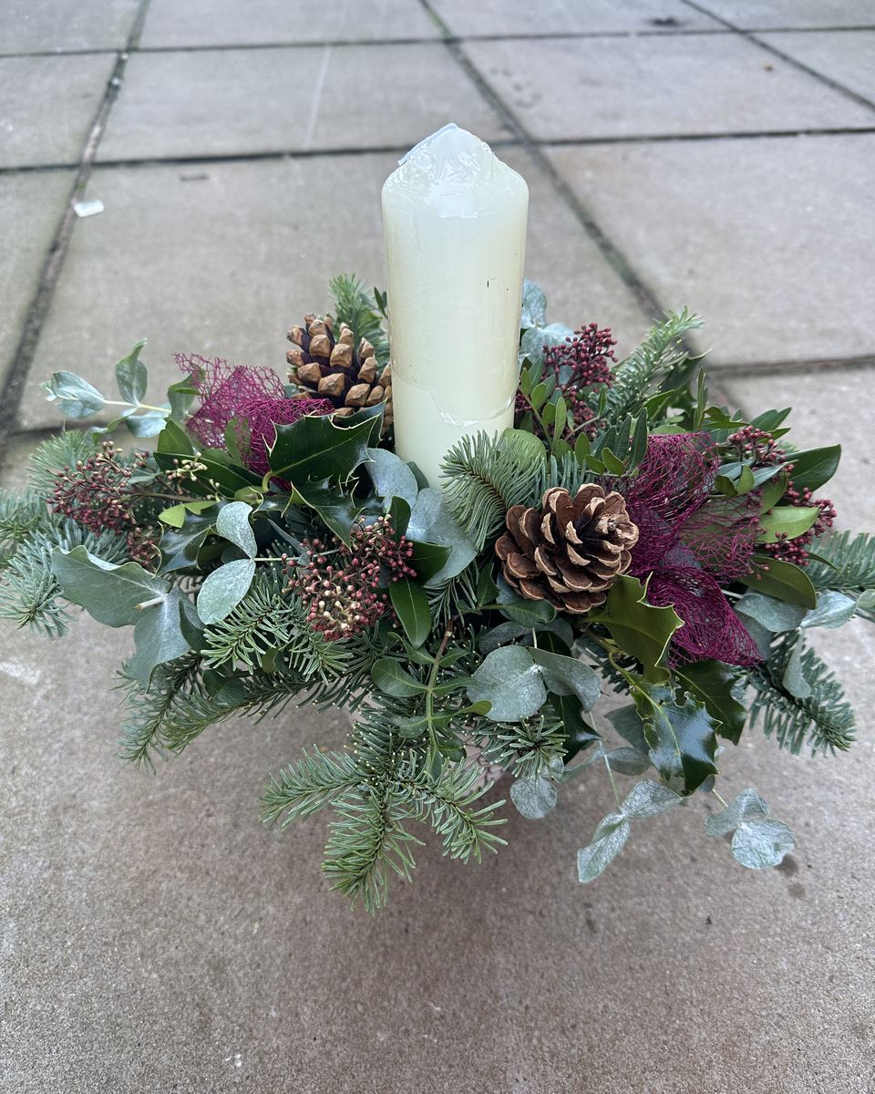 Christmas table centrepiece with a cream pillar candle, spruce, eucalyptus, pine cones and burgundy accents